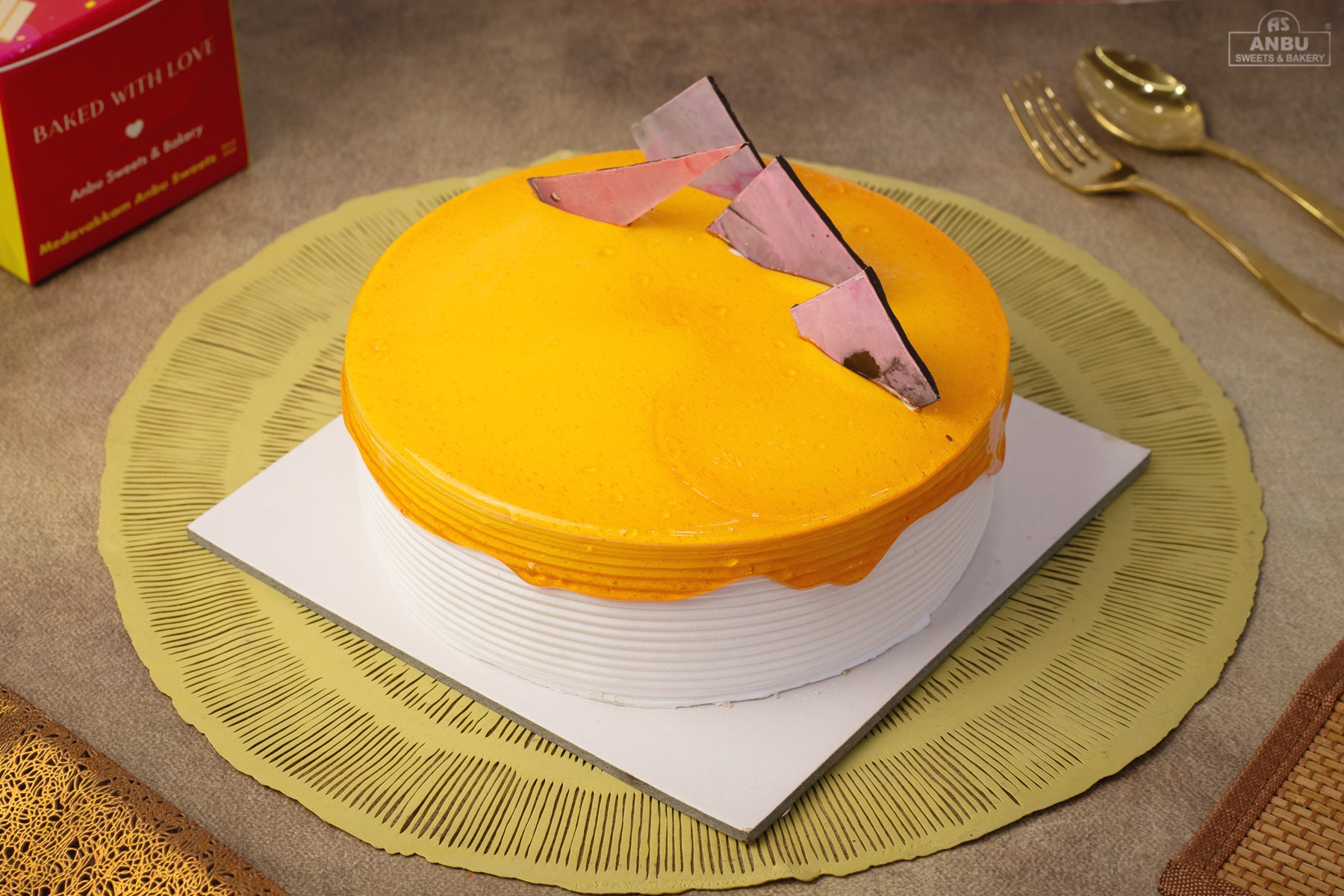 Yellow cake Butterscotch with a pink heart on a green placemat, surrounded by gold cutlery and a red box.